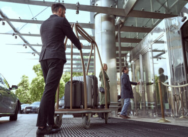 Couple of travellers proceeding inside of the hotel for a check-in while having their luggage deliverd by a porter